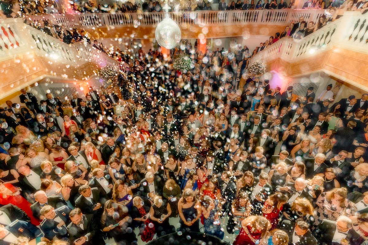 Overhead view of a formal gala filling the National Women's History Museum beneath a mirrored ball and falling confetti