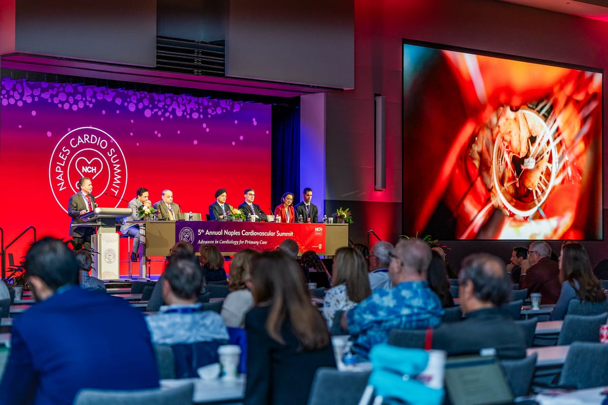 Naples Cardiovascular Summit panel beneath a red stage identity wall and clinical heart imagery
