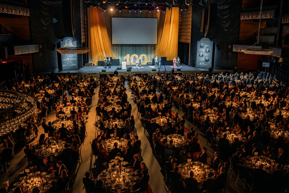 Large centennial gala filling a theater with candlelit dinner tables and a full stage program