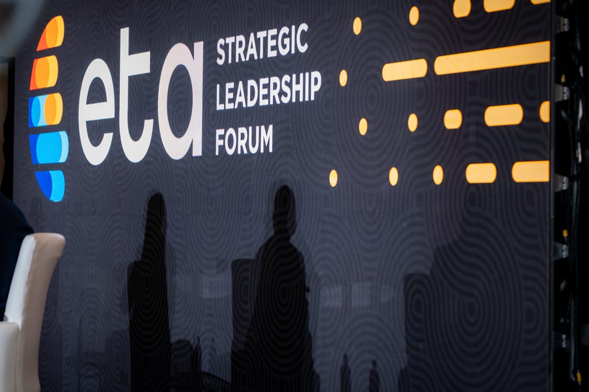 Attendee silhouettes beside a large strategic leadership forum identity wall