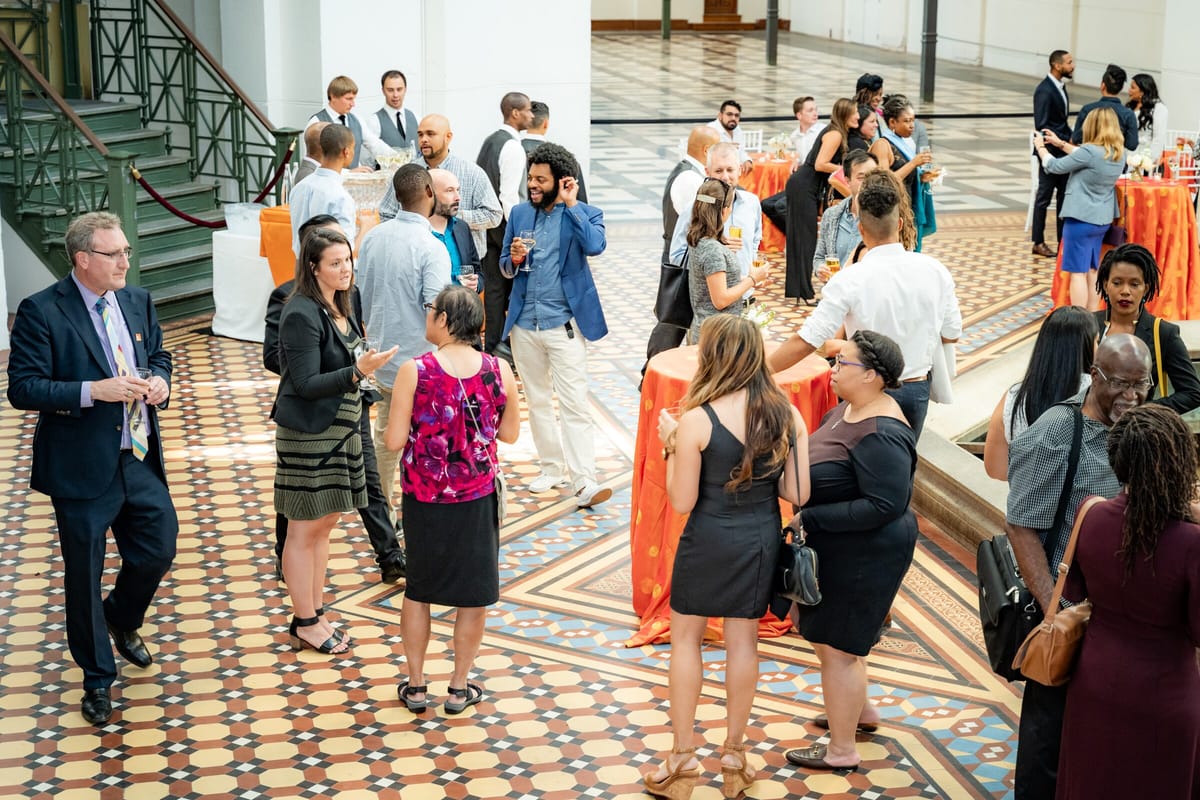 Scholars and faculty networking at an evening reception in a historic atrium with orange-draped cocktail tables